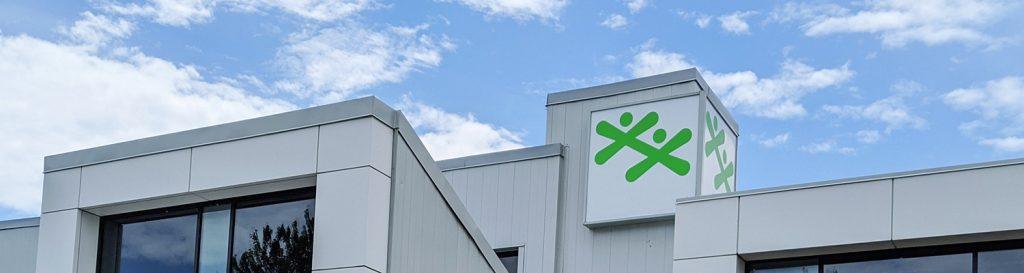 A modern white building features two green BGC logos prominently displayed on a square rooftop section against a blue sky with light clouds.