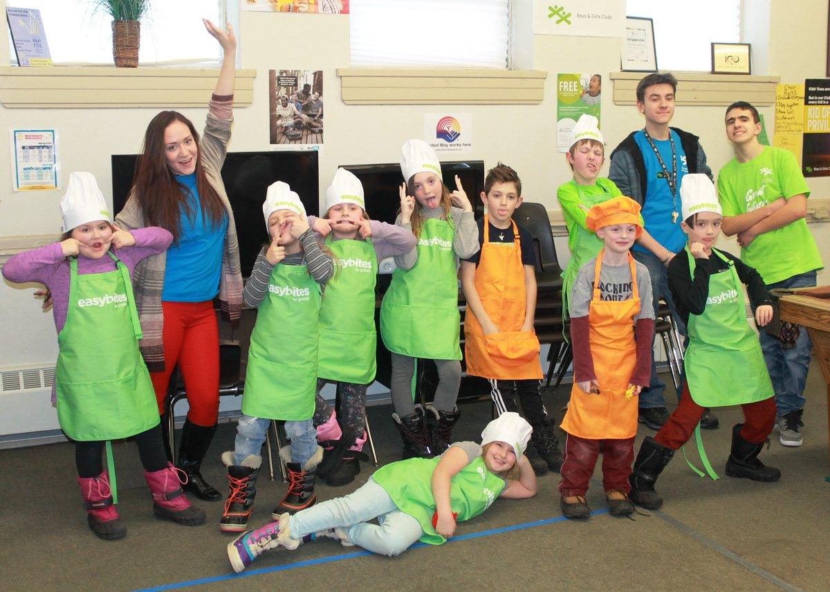 Group of children and adults wearing aprons and chef hats posing together.