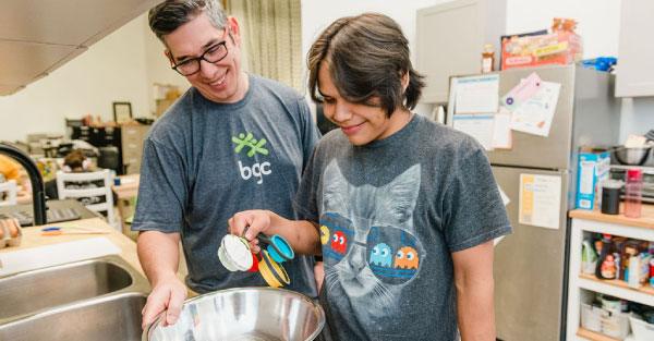 A BGC staff member and a youth participant smile while preparing ingredients together in the Easybites kitchen at BGC Club Airdrie.