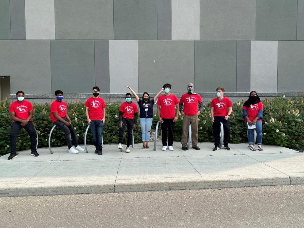 A group of people wearing red shirts and face masks pose for a photo outside a building.