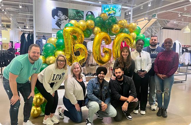 Group of people posing with large gold "BGC" balloons in a clothing store.