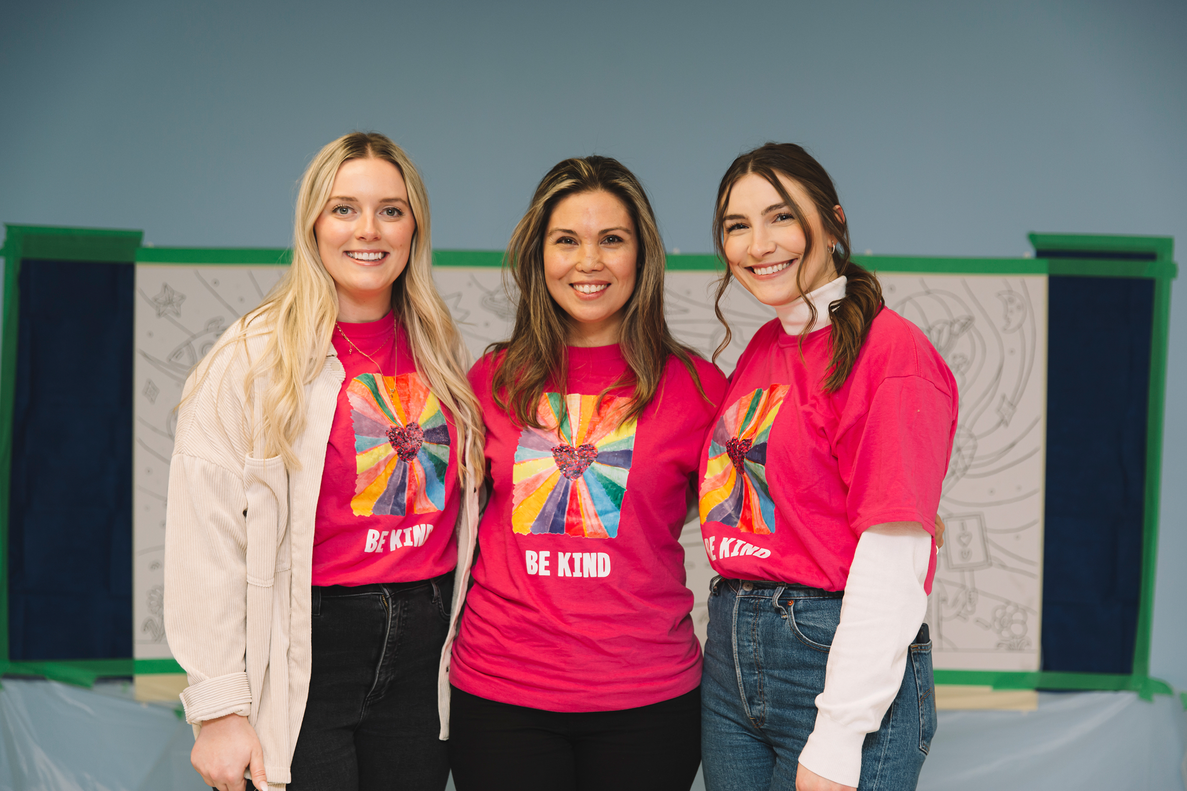 Three women smiling and wearing bright pink “Be Kind” t-shirts during BGC Canada’s mental health awareness event