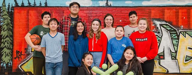 Group of children and youth standing together in front of a graffiti mural.