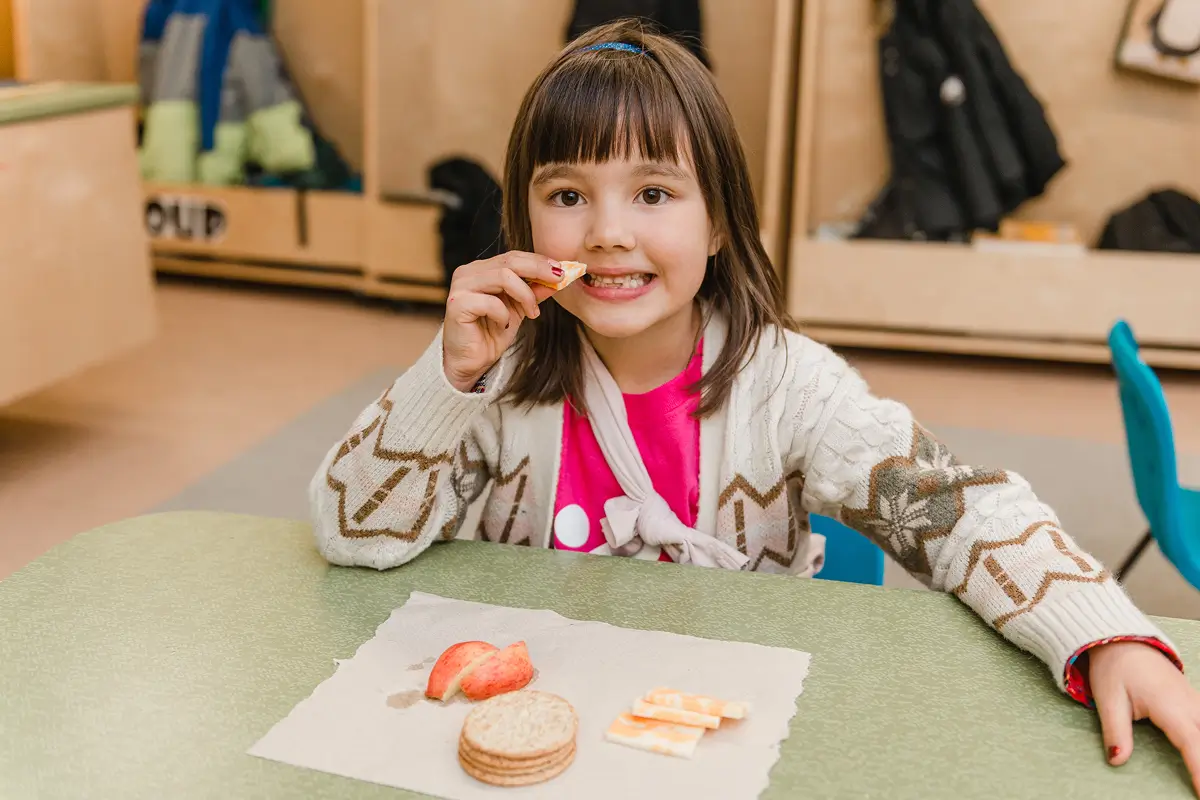 Young girl smiling while eating healthy snacks at a table