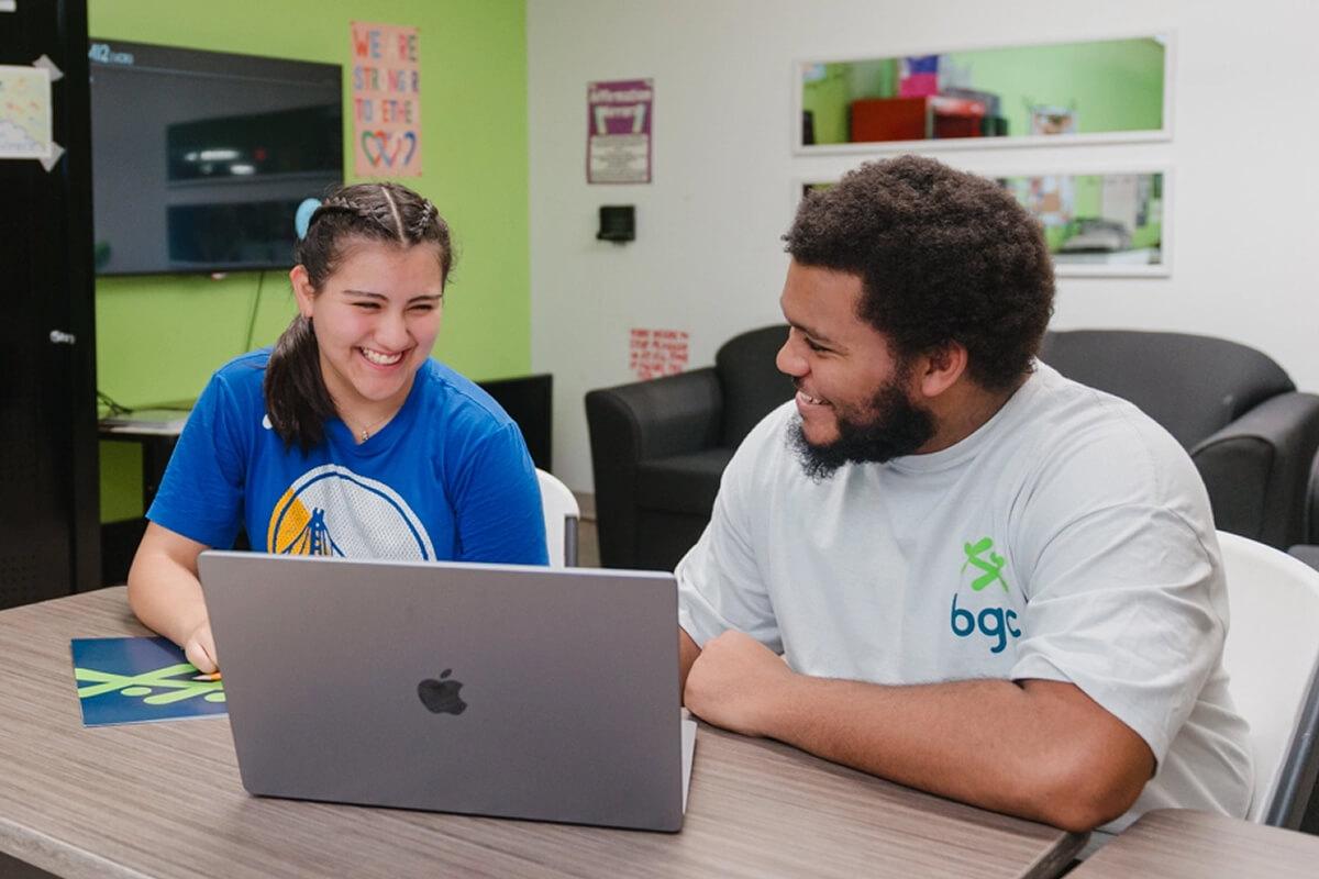 Young man and woman smiling while looking at a laptop.