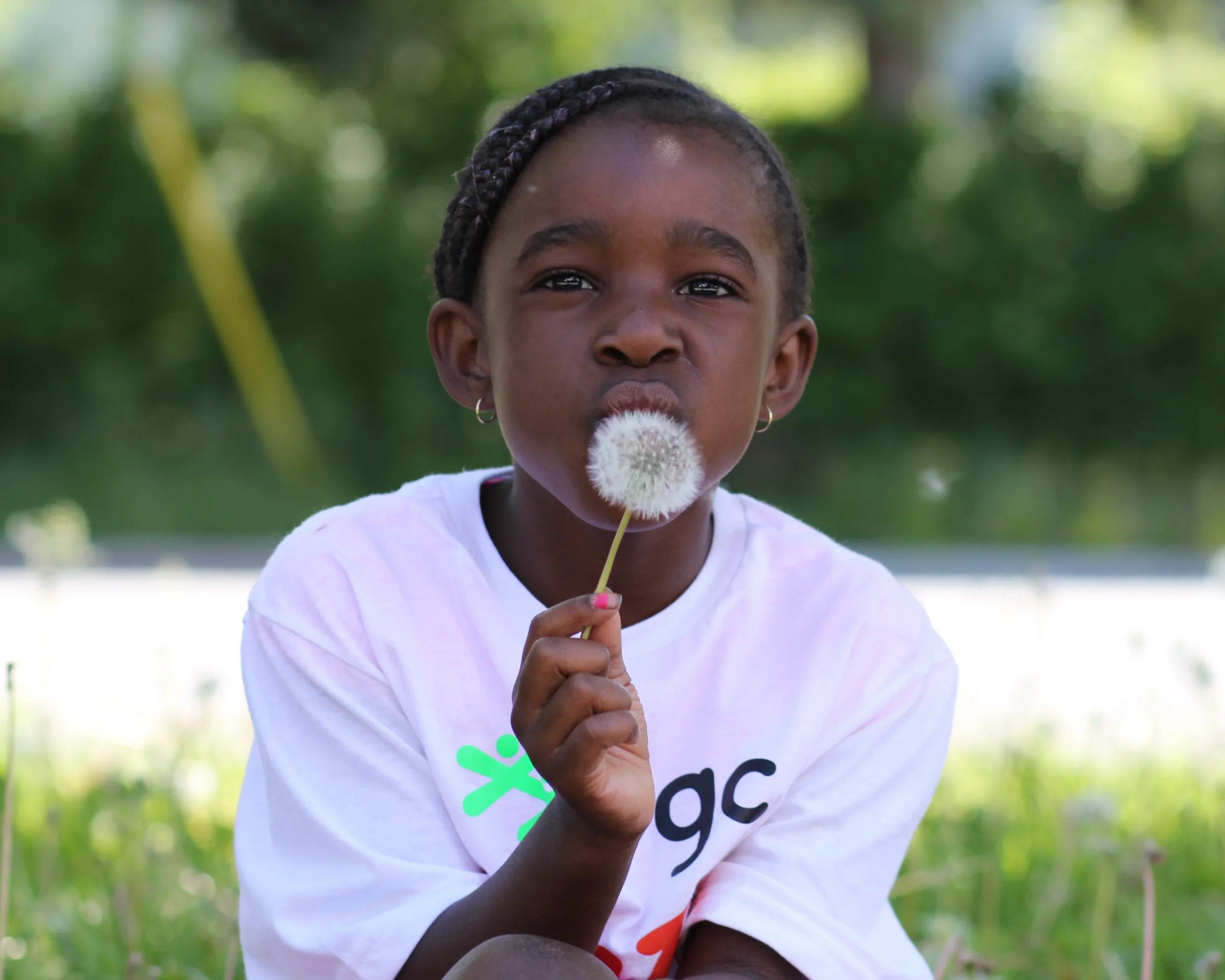 Young girl blowing on a dandelion seed head outdoors.