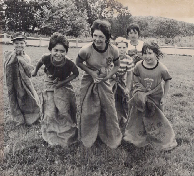 A vintage black and white photo of smiling children competing in an outdoor potato sack race.