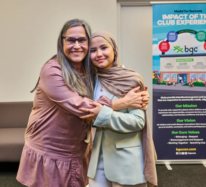 Two women embracing at a BGC event, standing in front of an informational banner.