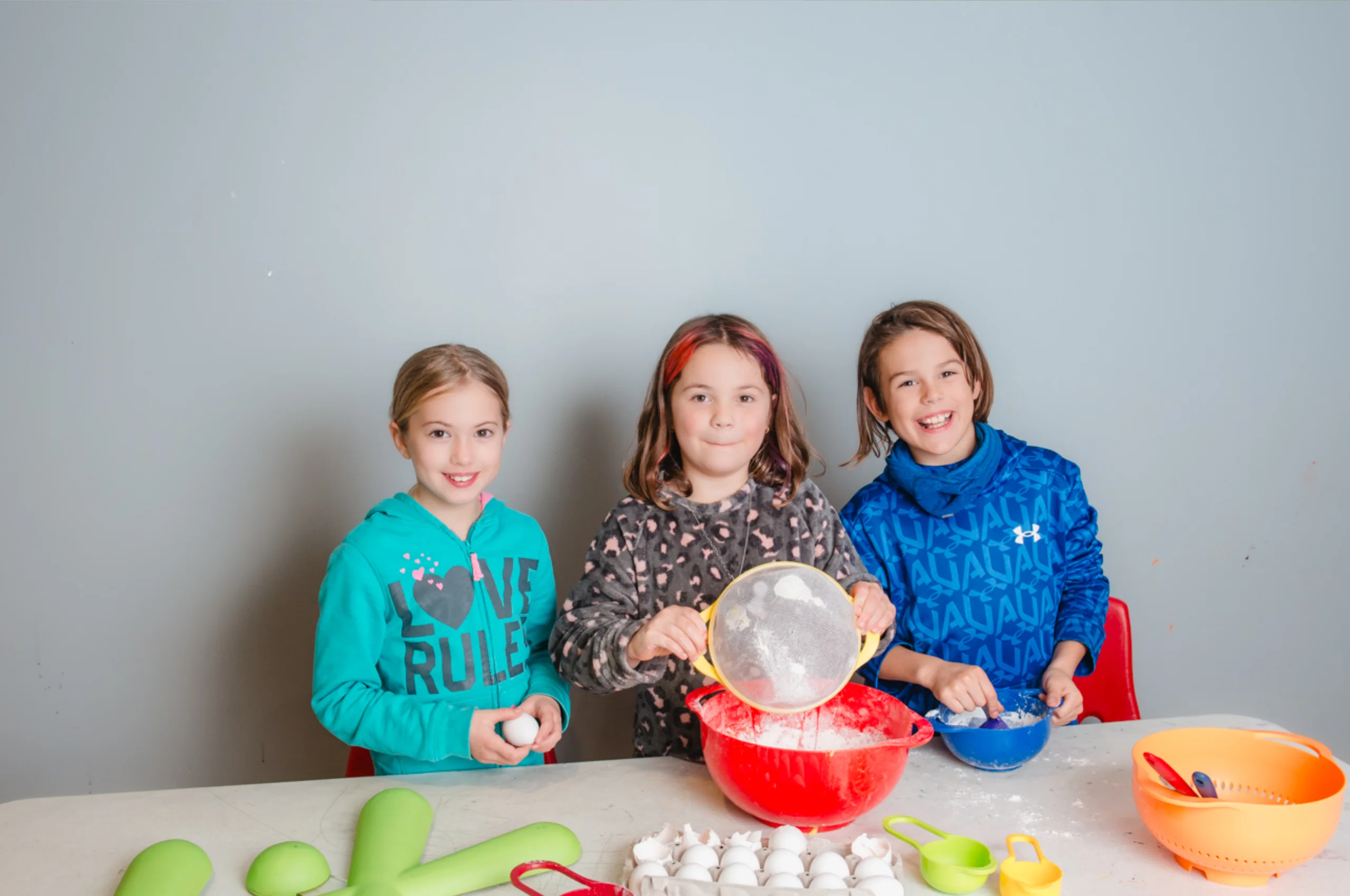 Three children preparing food together at a table during a hands-on cooking activity.