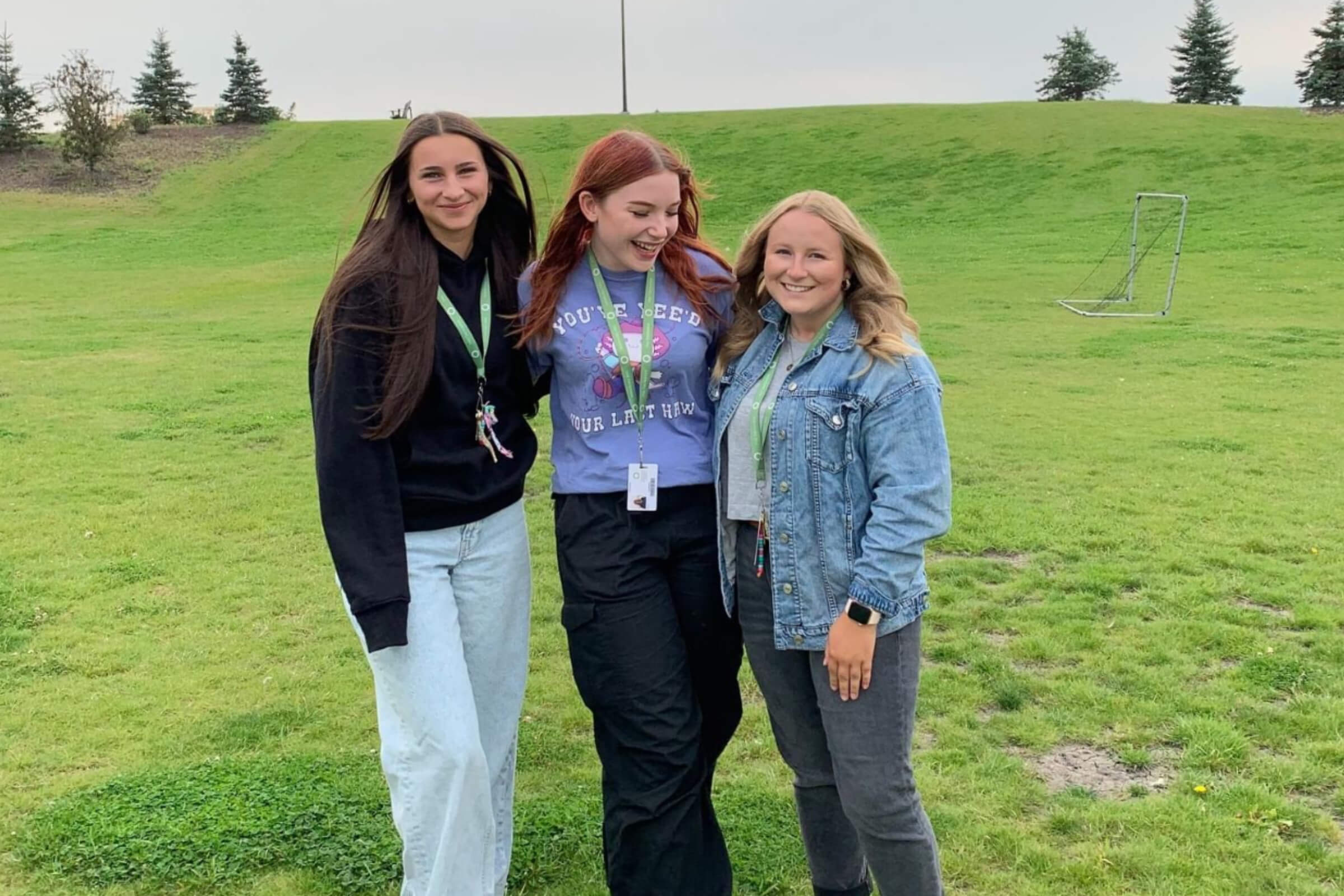 Yaël standing outdoors with two other teens on a grassy field.