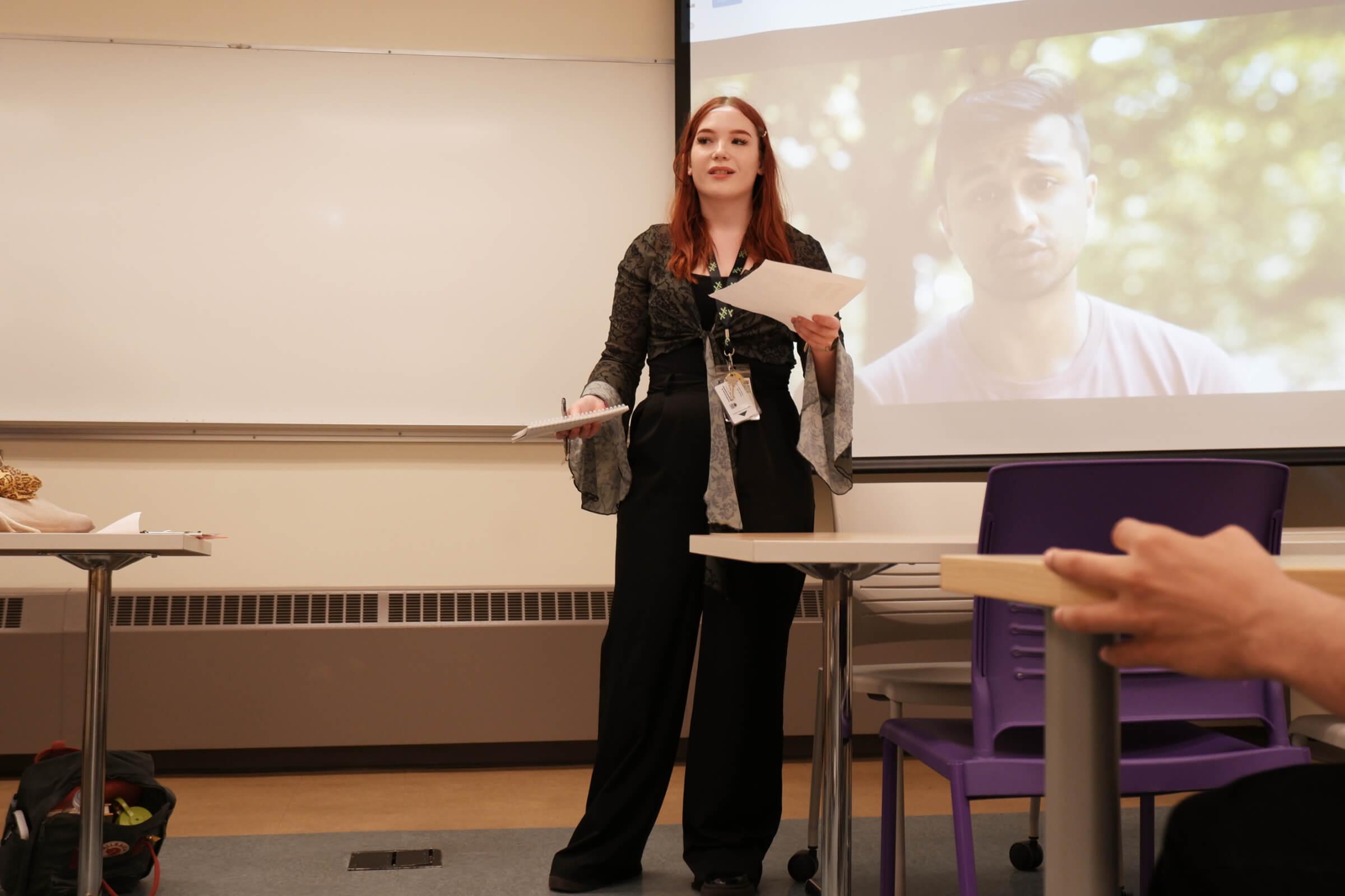 Yaël speaking at the front of a classroom during a presentation.