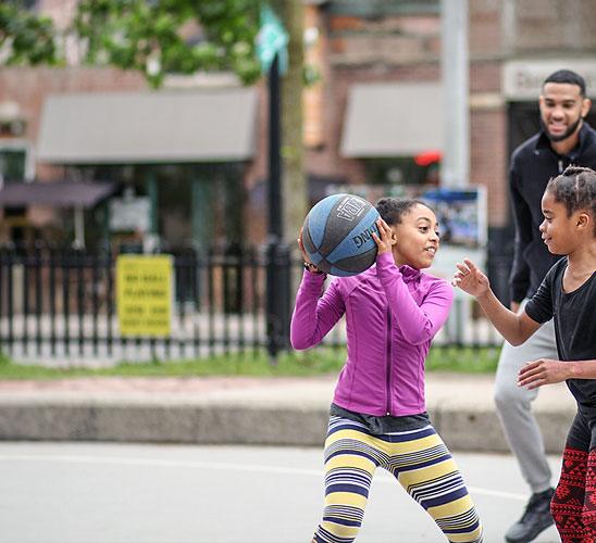 Young girl holding a basketball on an outdoor court.