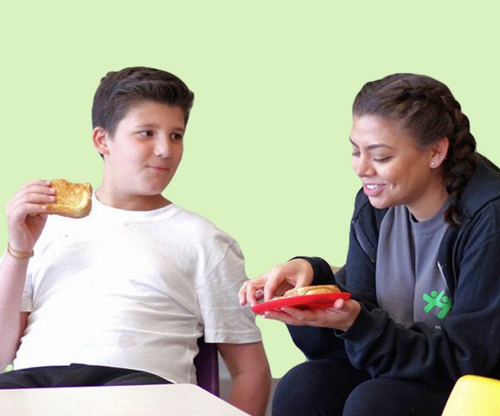 A young boy and a woman sit together at a table sharing and eating toasted sandwiches.