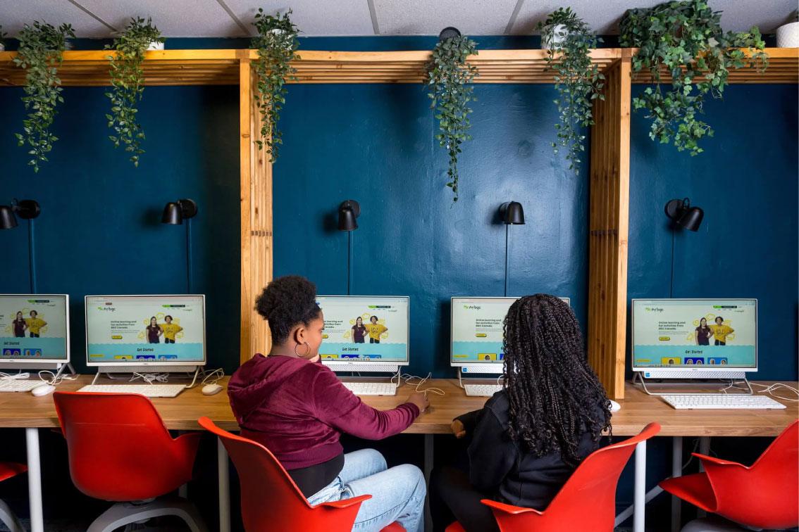 Two youth seated in a computer lab using desktop computers to access the MyBGC online learning platform, with greenery above the workstations
