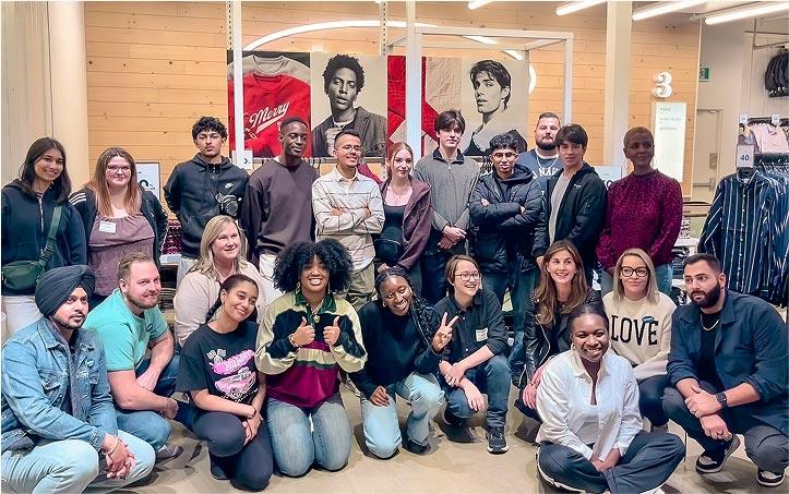 Large group of diverse youth and adults posing together inside a clothing store.