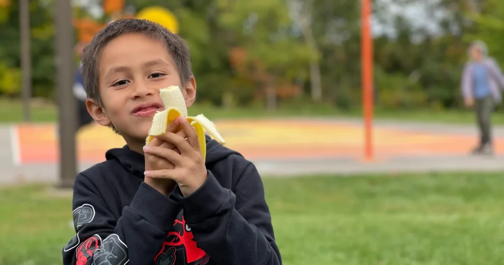 Child eating a banana outdoors at a playground.
