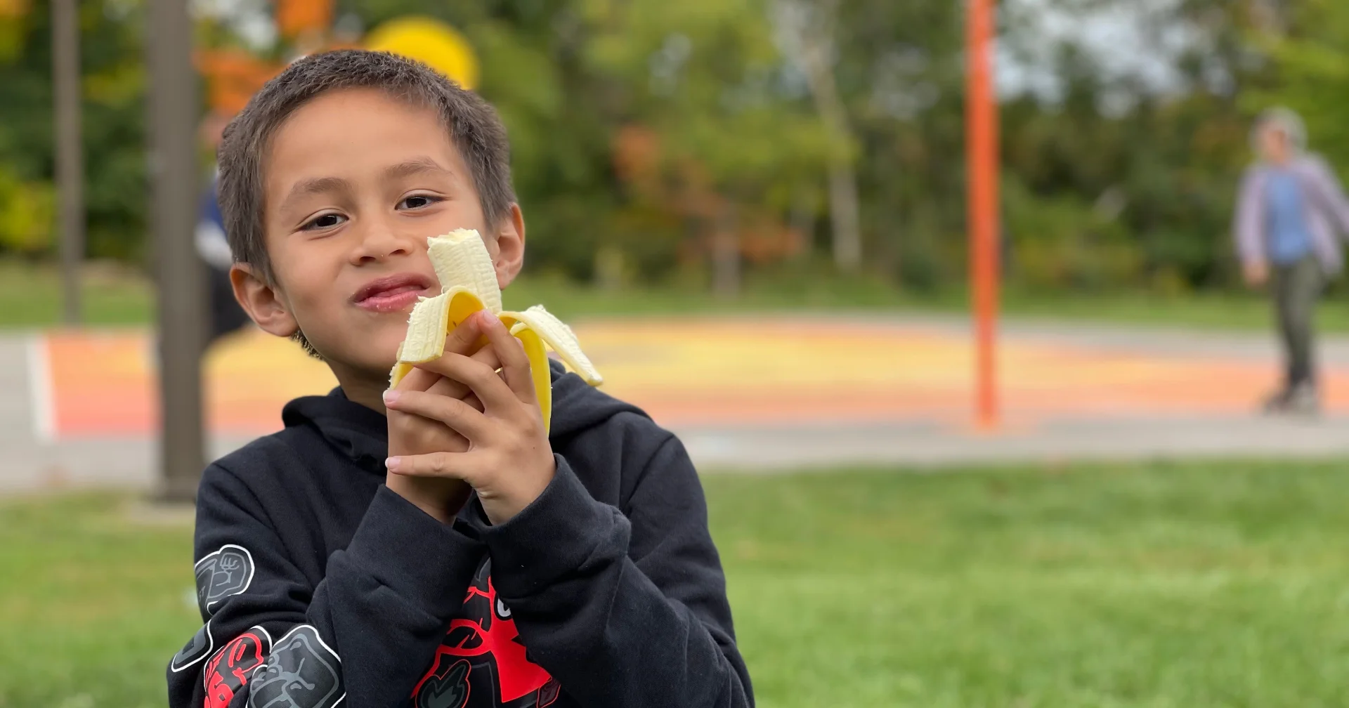 Child eating a banana outdoors at a playground.