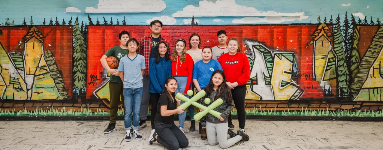 Youth group smiling and holding BGC symbols in front of a painted wall