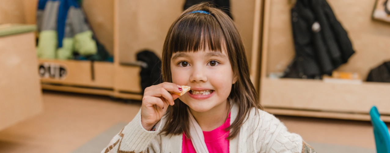 Young girl smiling while eating healthy snacks at a table